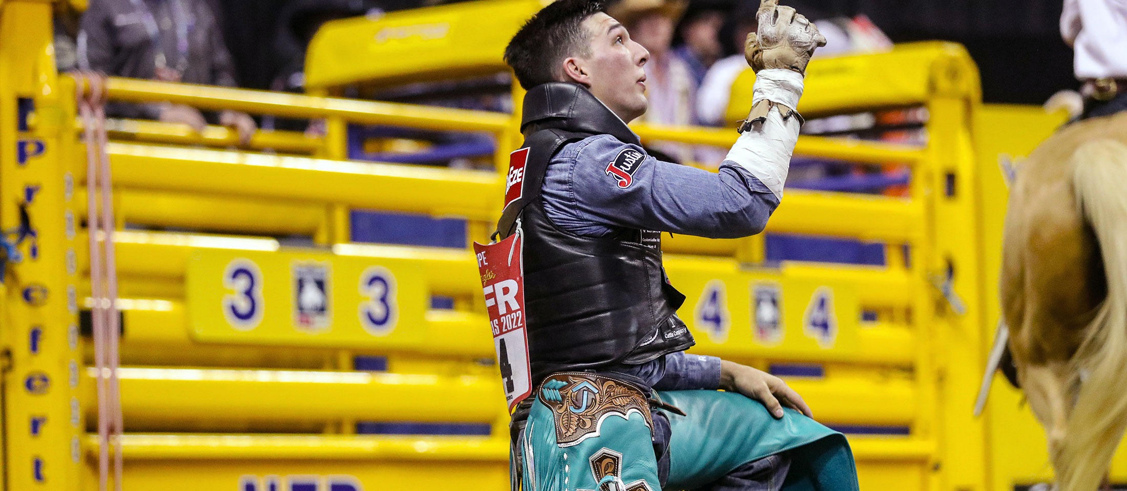 Jess Pope kneeling on one knee pointing at the sky with one hand in a rodeo arena.